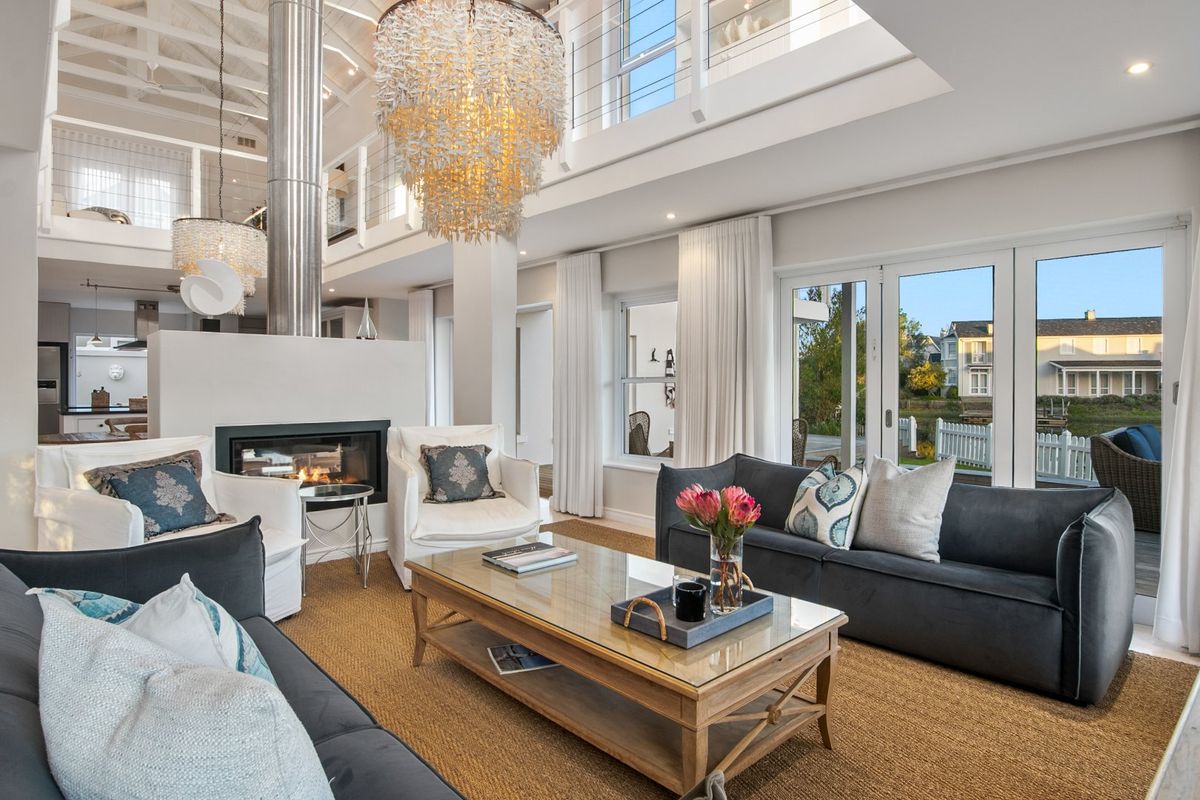 Spacious double-volume living area featuring a modern double-sided fireplace, mezzanine level, and large glass doors opening to the exterior.