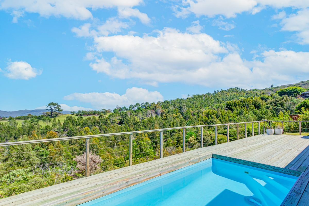 An elevated swimming pool with timber decking and wire balustrade, offering expansive views of the surrounding lush green landscape.