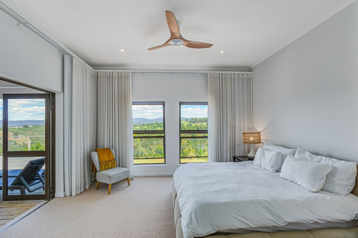 Spacious bedroom featuring neutral carpeting, a modern ceiling fan, and large windows with floor-to-ceiling curtains, offering scenic views and access to a private balcony.