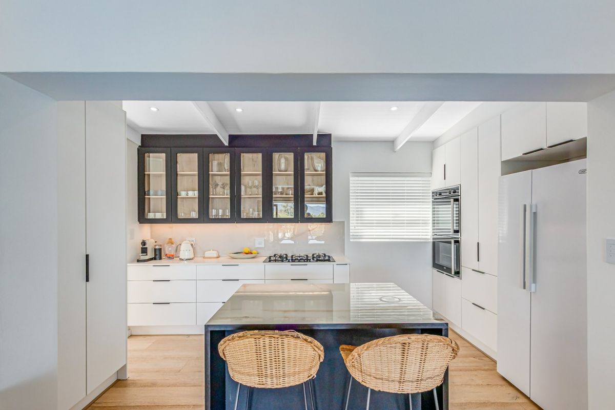 Modern kitchen featuring a central island, gas cooktop, built-in double oven, and a mix of white and dark glass-front cabinetry with recessed lighting.