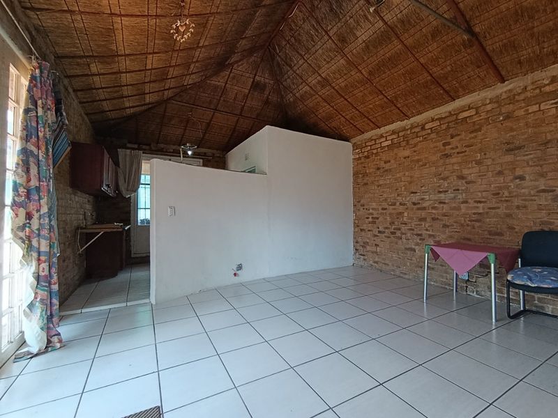 Open-plan living area featuring exposed brick walls, a traditional thatched ceiling, and ceramic tiled flooring, with an integrated kitchen space.