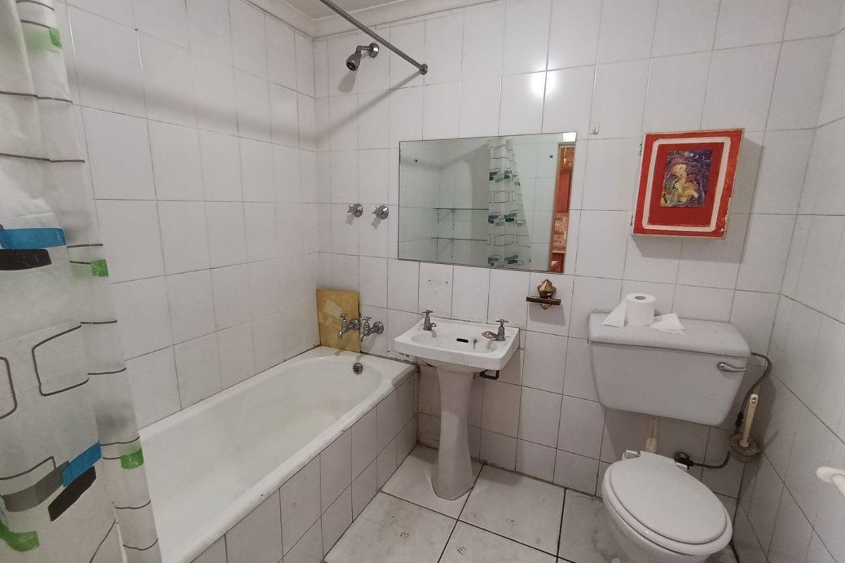 A dated bathroom featuring a bathtub, pedestal basin, and toilet with fully tiled walls and flooring, requiring cosmetic updates and maintenance.