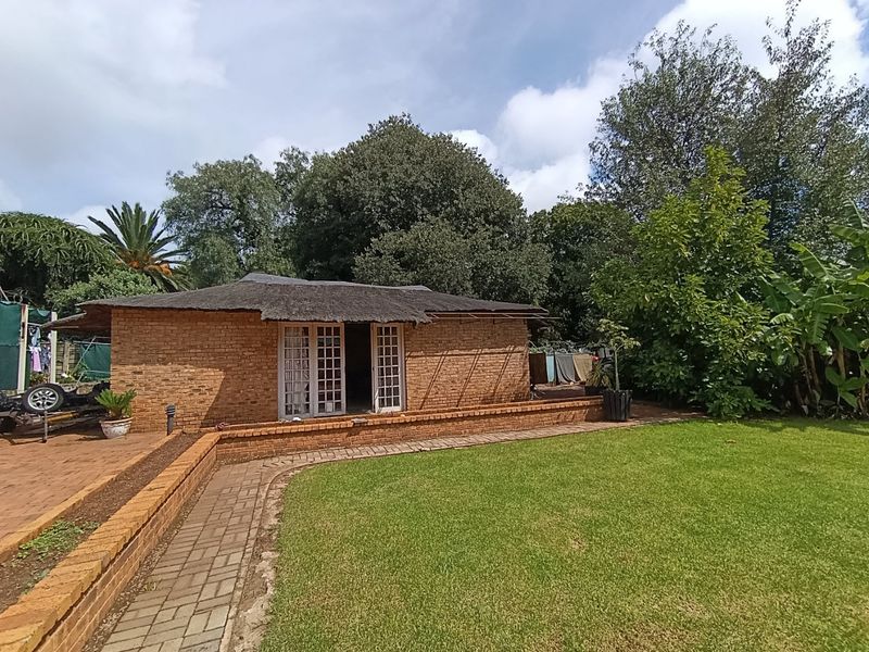 Rear view of a brick-built structure featuring a traditional thatch roof, french doors, and a surrounding brick-paved patio area set within a garden.