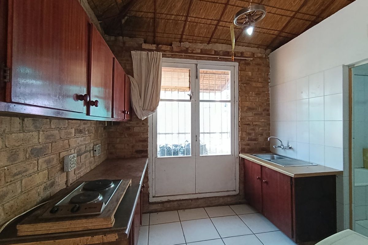 Rustic kitchen featuring exposed brick walls, a traditional thatch ceiling, built-in wooden cabinetry, an electric hob, and direct access to the exterior.