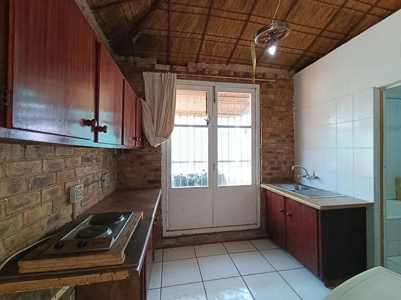 Rustic kitchen featuring exposed brick walls, a traditional thatch ceiling, built-in wooden cabinetry, an electric hob, and direct access to the exterior.