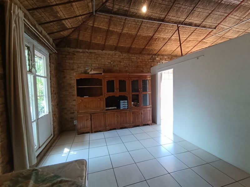 Living area featuring rustic exposed brick walls, a traditional thatched ceiling, and tiled flooring with access to the exterior through french doors.