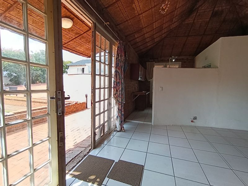 Open plan living area featuring tiled floors, exposed thatch ceiling, and large french doors providing direct access to the outdoor patio area.