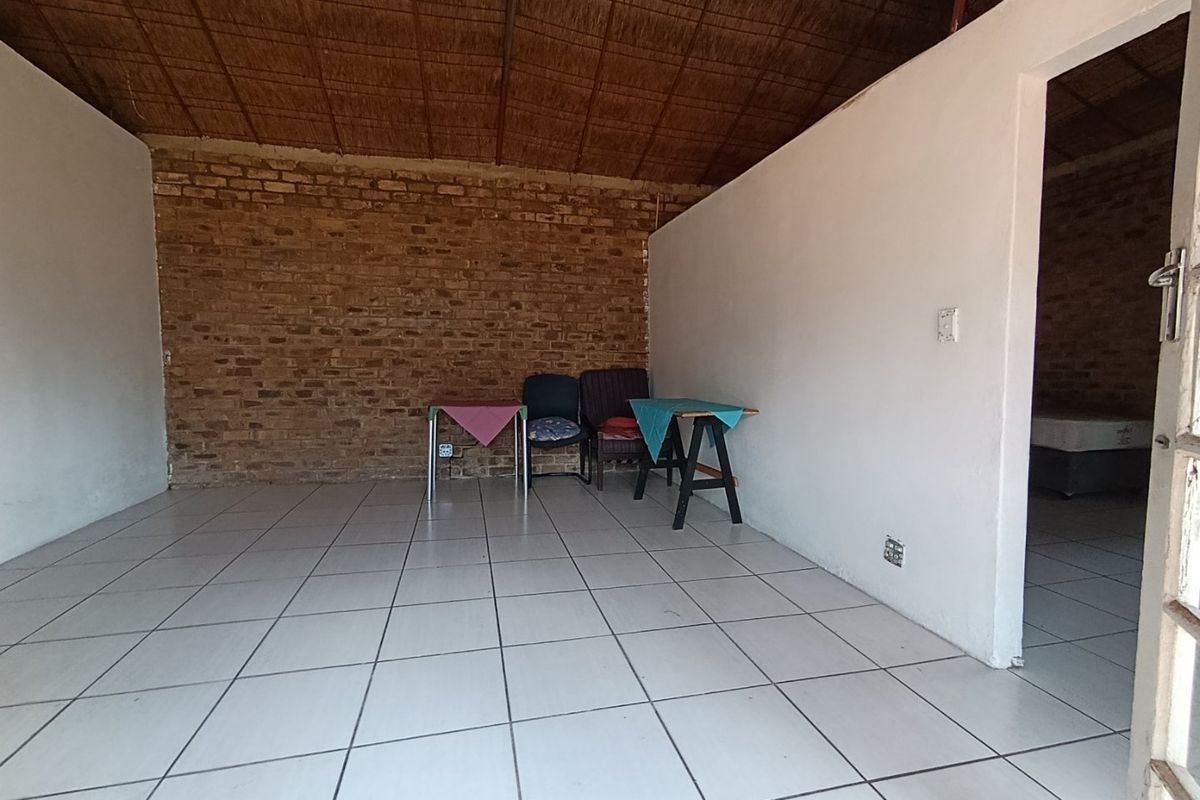 An open-plan living area featuring exposed brick walls, a traditional thatched ceiling, and neutral tiled flooring.
