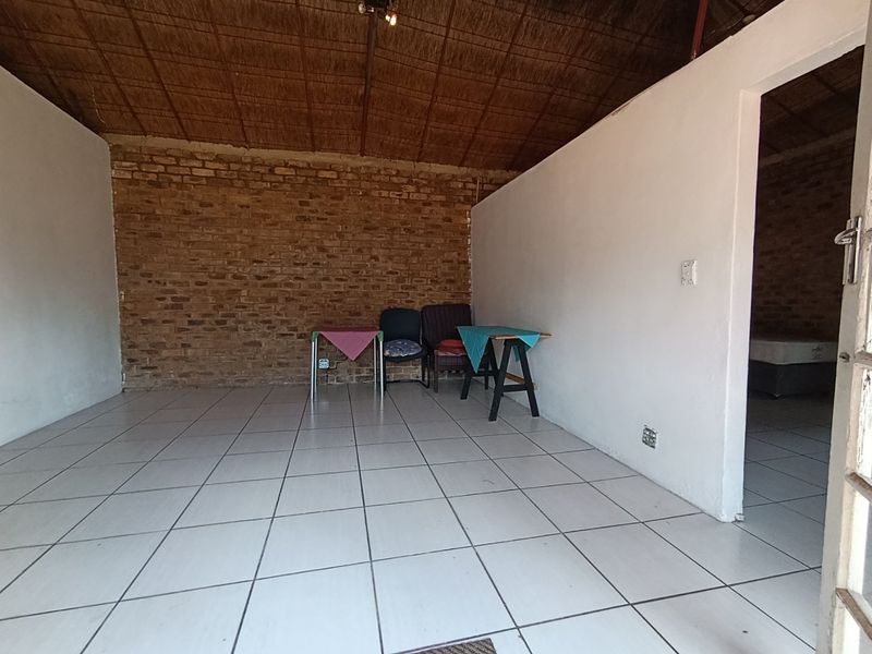 An open-plan living area featuring exposed brick walls, a traditional thatched ceiling, and neutral tiled flooring.