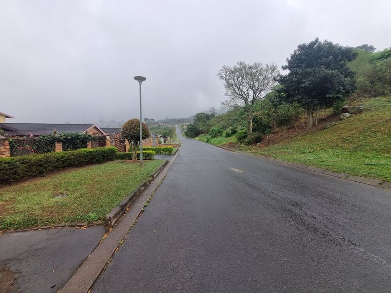 A view of the residential street approach, featuring paved road, concrete curbing, and established landscaped verges in a quiet neighborhood setting.
