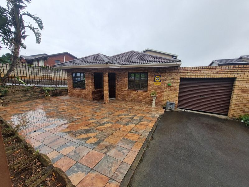 Front view of a face brick house featuring a tiled driveway, single garage, and secure perimeter fencing.