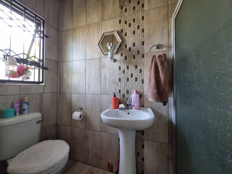 A functional bathroom featuring a pedestal basin, toilet, and shower enclosure with neutral wood-look wall tiling.