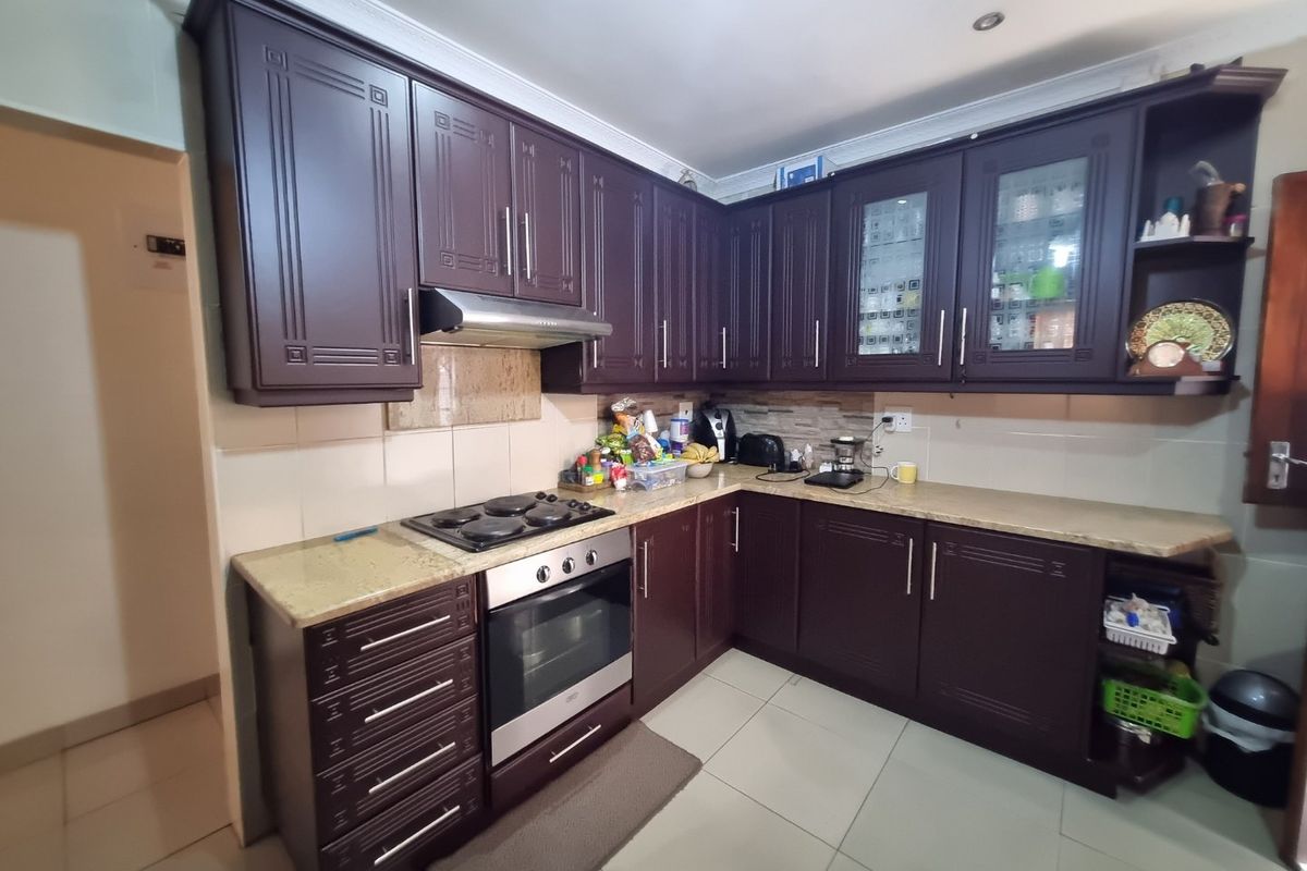 A functional kitchen featuring dark wood cabinetry, granite countertops, a built-in oven, and an electric hob with a stainless steel extractor fan.
