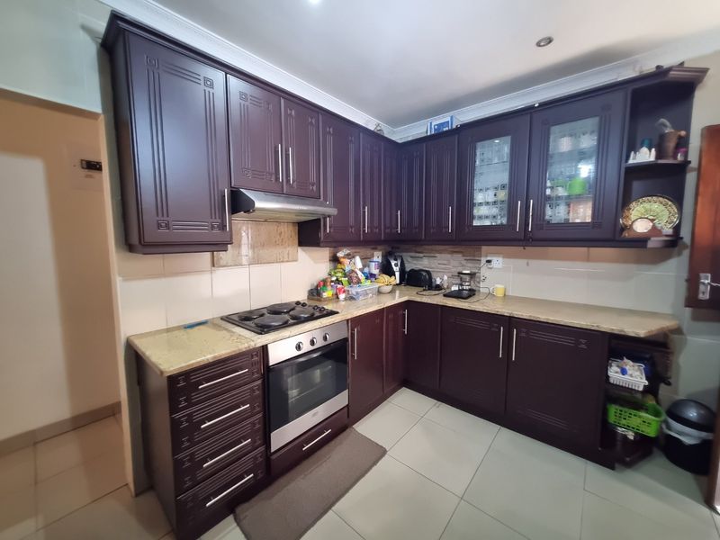 A functional kitchen featuring dark wood cabinetry, granite countertops, a built-in oven, and an electric hob with a stainless steel extractor fan.