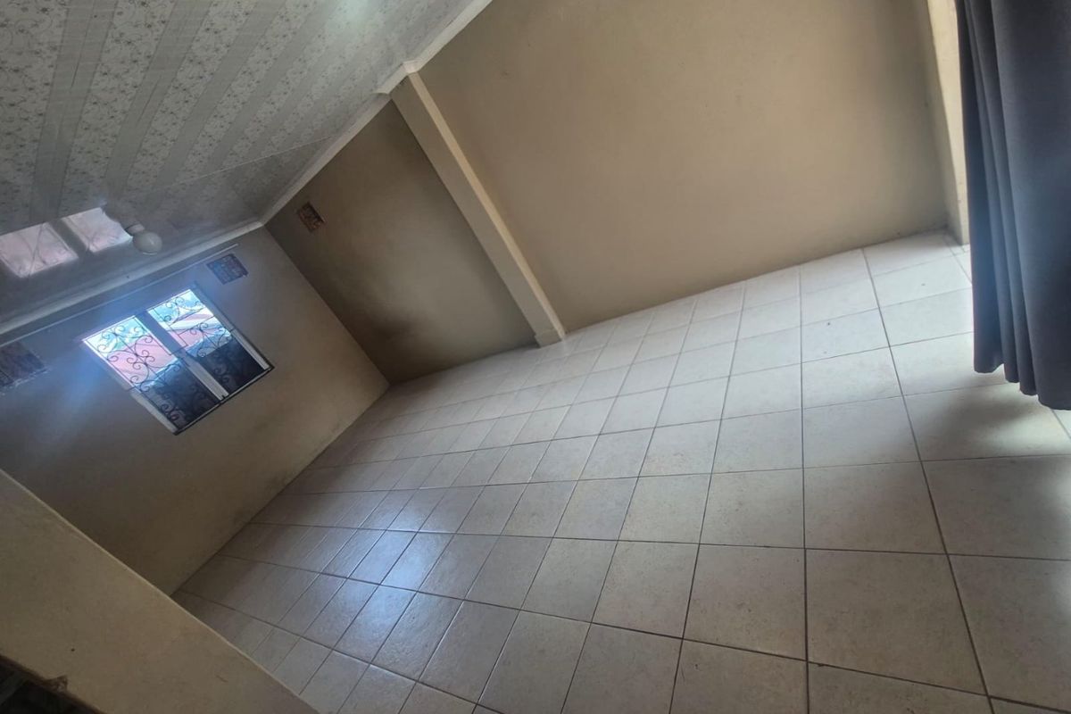 An empty bedroom featuring tiled flooring, a coved ceiling, and a window fitted with security bars.