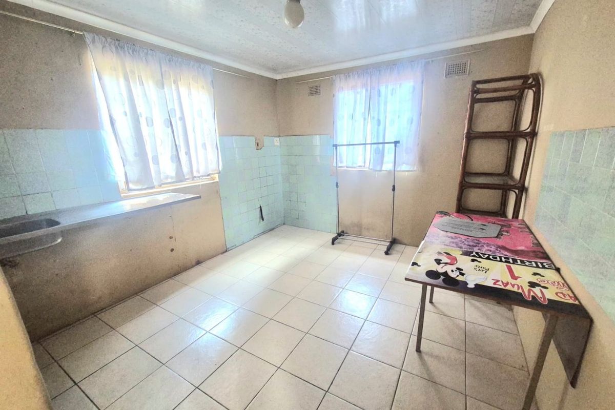 A dated kitchen area featuring tiled flooring, a built-in counter with a stainless steel sink, and tiled splashbacks, requiring cosmetic updates.