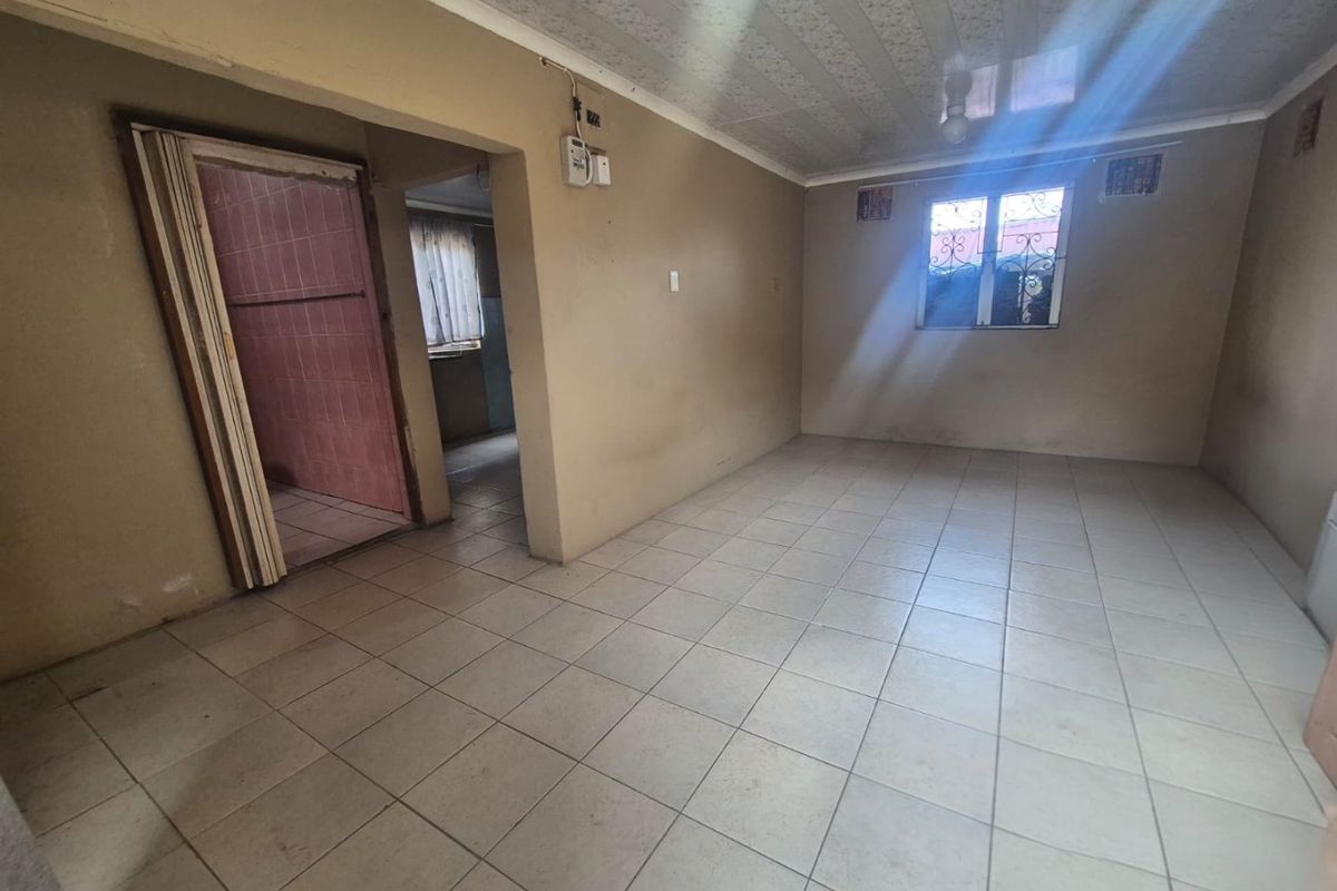 An empty living area featuring tiled flooring, security bars on the windows, and a folding door leading to an adjacent room.