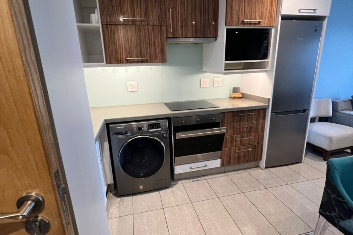 Modern compact kitchen featuring wood-grain cabinetry, stone countertops, glass splashback, and integrated appliances including an oven, hob, and extractor fan.