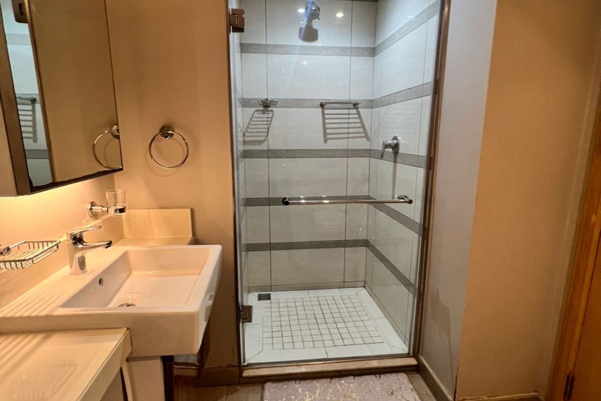 A modern, well-maintained bathroom featuring a wall-mounted basin, a glass-enclosed shower with tiled finishes, and contemporary fixtures.