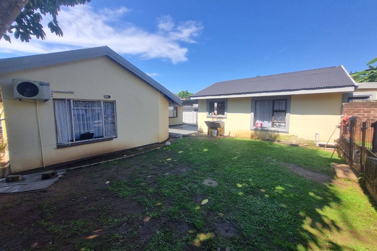 Rear exterior view of the property featuring a lawn area, external utility sink, and security-fitted windows on the building facade.