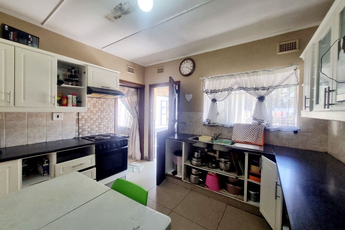 A functional kitchen featuring built-in cabinetry, an electric stove with extractor fan, and tiled backsplash, requiring some maintenance and cosmetic updates.