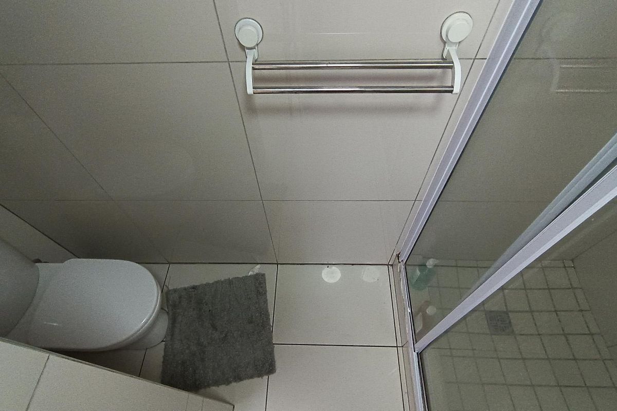 A compact bathroom featuring a toilet, a glass-enclosed shower, and neutral wall and floor tiling.