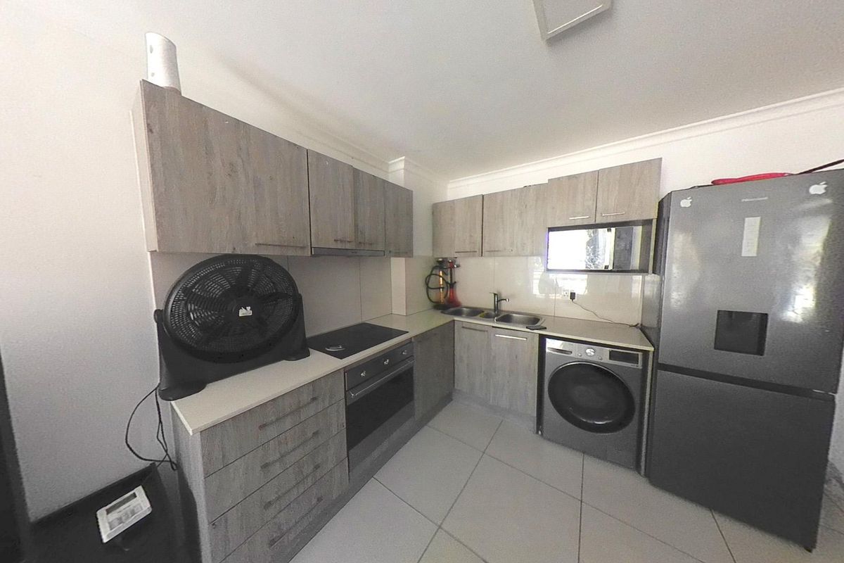 A functional kitchen featuring modern wood-look laminate cabinetry, built-in oven, electric hob, and integrated laundry facilities with tiled flooring throughout.