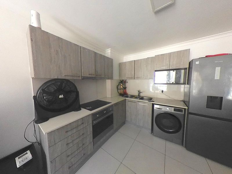 A functional kitchen featuring modern wood-look laminate cabinetry, built-in oven, electric hob, and integrated laundry facilities with tiled flooring throughout.