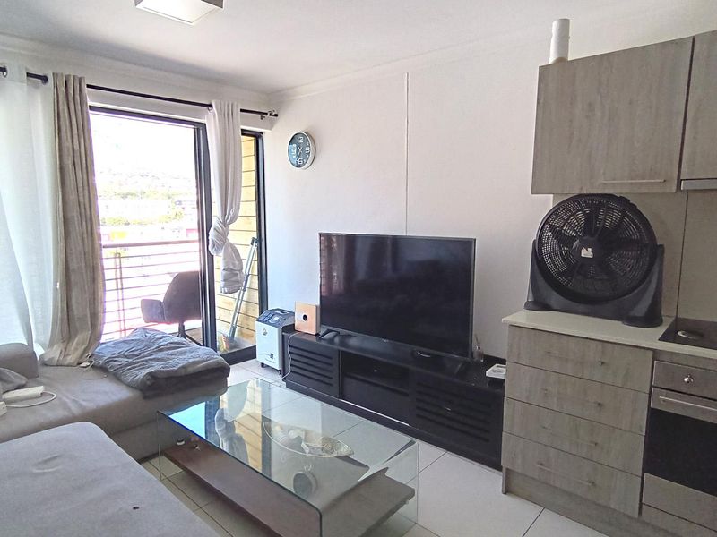 Open-plan living area featuring a compact kitchen with built-in cabinetry, oven, and hob, leading directly to a balcony through sliding glass doors.