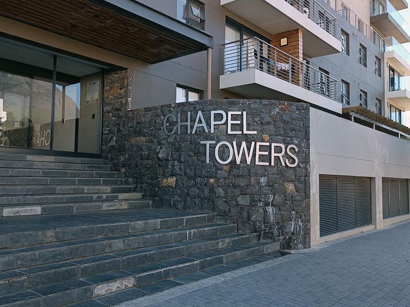 The main entrance of Chapel Towers apartment complex, featuring stone cladding, modern glass doors, and stone steps leading to the building.