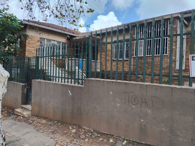 Front elevation of a brick house featuring security fencing and bars, with a concrete boundary wall showing visible graffiti and signs of weathering.