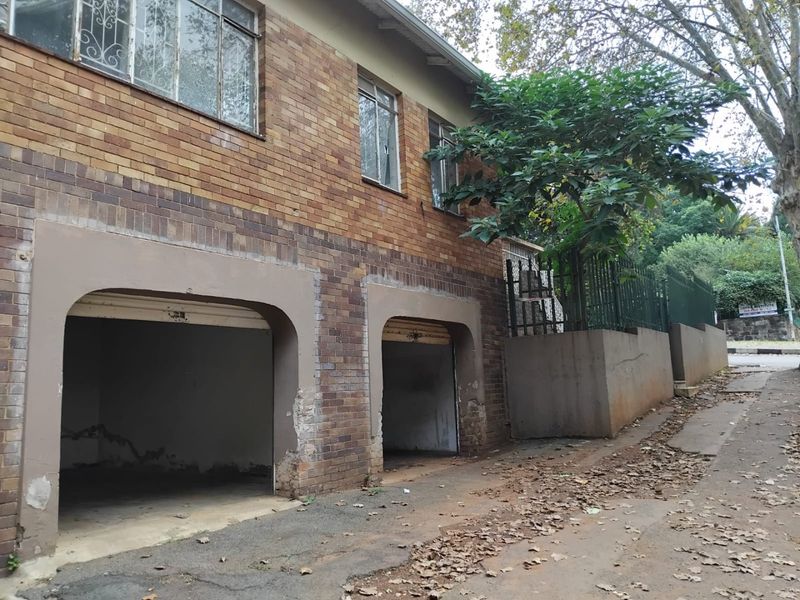 Exterior view of a double garage featuring a brick facade with visible wear and concrete retaining walls along the street frontage.
