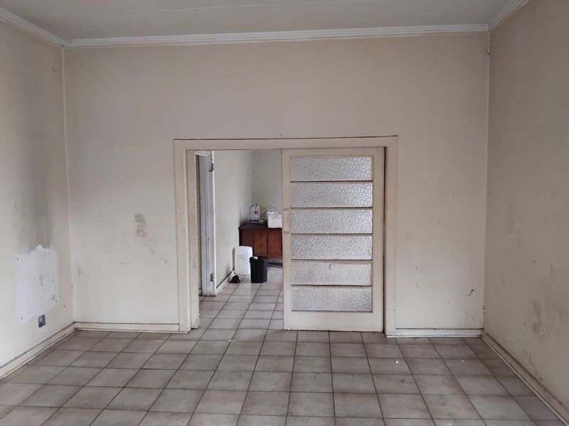 An empty living room featuring ceramic floor tiles and a sliding door with textured glass panels, requiring cosmetic updates and wall repairs.