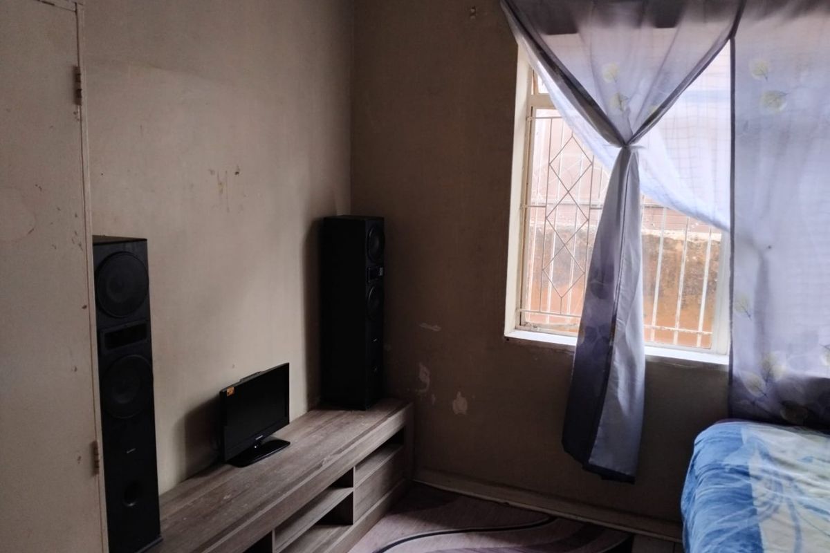 A bedroom featuring a window with security bars and visible wear on the wall finishes.