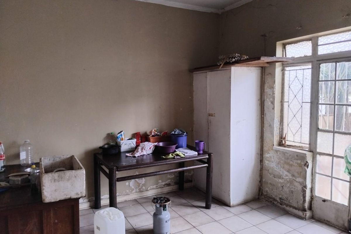 A basic kitchen area featuring tiled flooring and a built-in cupboard, currently showing significant wear to the wall finishes and plaster.