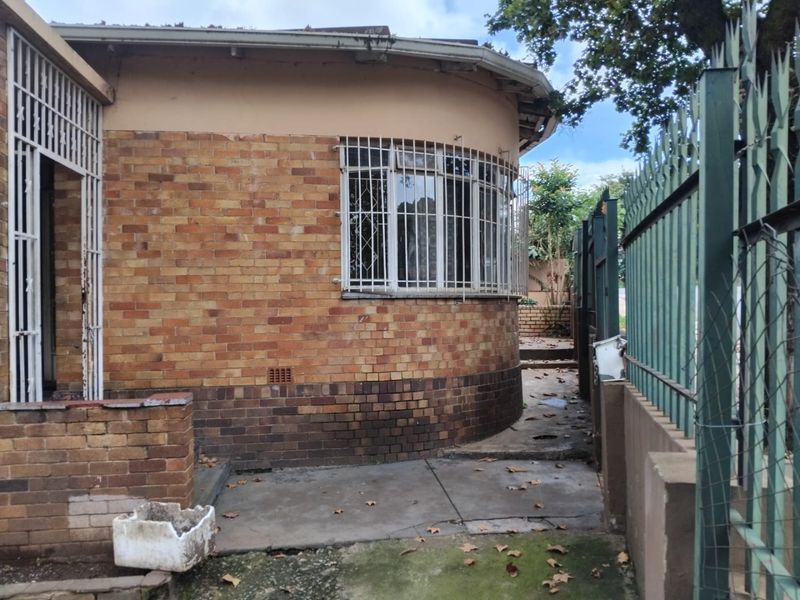 Rear exterior view of a brick house featuring a curved wall, security bars on windows, and concrete paving along the perimeter fence.