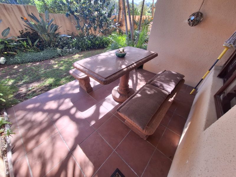 A paved outdoor patio area featuring a built-in stone table and bench set, adjacent to a landscaped garden space.