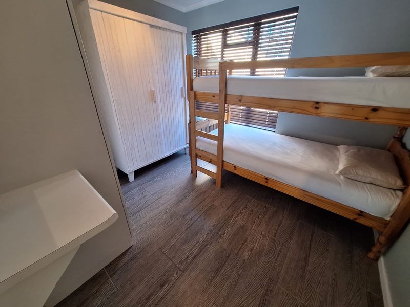 A bedroom featuring wood-look tile flooring and venetian blinds, providing a functional and neutral space.