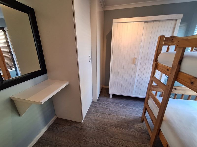 A bedroom featuring built-in cupboards, modern laminate flooring, and a wall-mounted shelf, providing functional storage and a clean aesthetic.