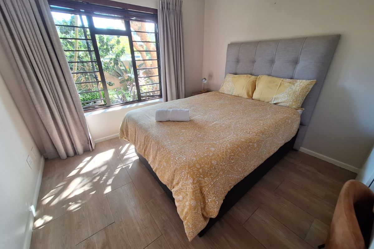 A well-lit bedroom featuring modern tiled flooring and a large window with security bars, offering a bright and comfortable living space.