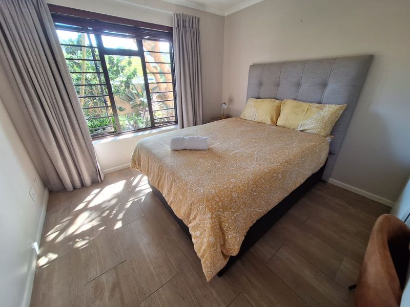 A well-lit bedroom featuring modern tiled flooring and a large window with security bars, offering a bright and comfortable living space.