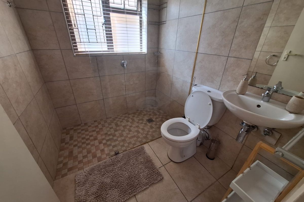 A functional bathroom featuring a walk-in shower, pedestal basin, and toilet, finished with neutral ceramic wall and floor tiles.