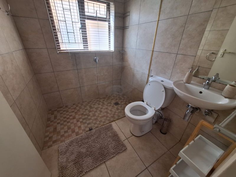 A functional bathroom featuring a walk-in shower, pedestal basin, and toilet, finished with neutral ceramic wall and floor tiles.