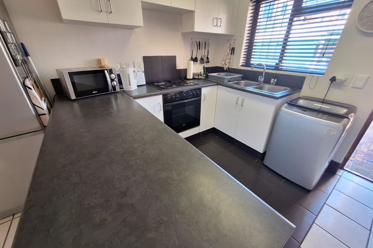 A functional kitchen featuring white cabinetry, dark laminate countertops, a built-in oven with gas hob, and a stainless steel double sink.