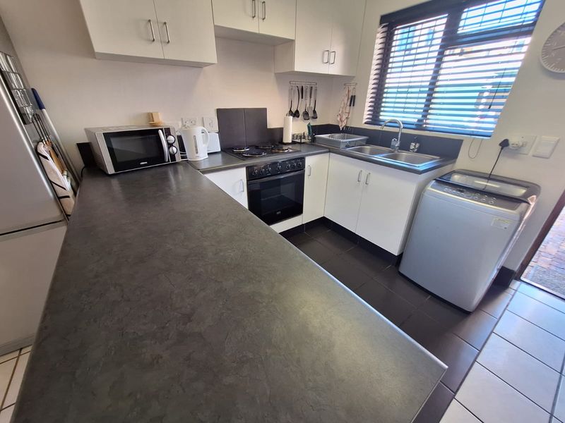 A functional kitchen featuring white cabinetry, dark laminate countertops, a built-in oven with gas hob, and a stainless steel double sink.