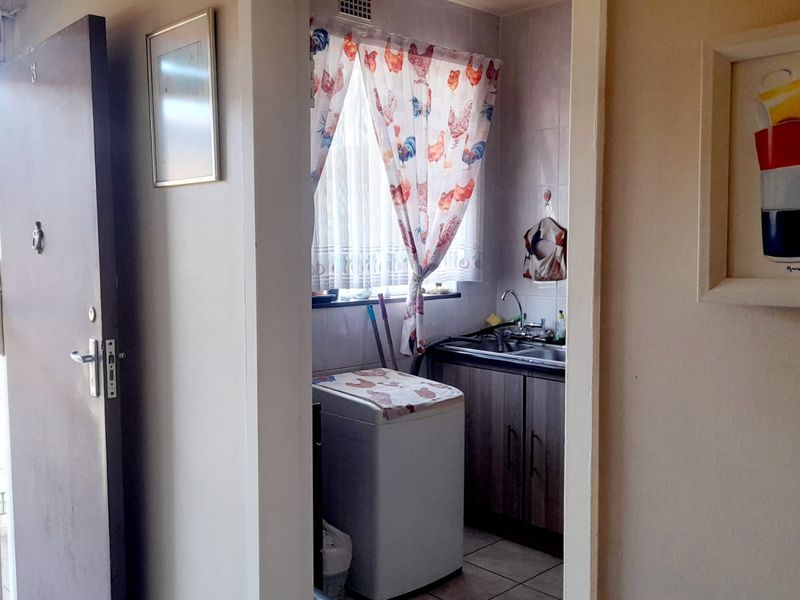 A functional laundry area featuring tiled walls and flooring, a stainless steel sink, and built-in cabinetry, accessible via a hallway.