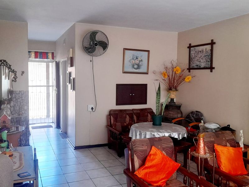 A living room area featuring tiled flooring, a wall-mounted fan, and access to an entrance with a security gate.