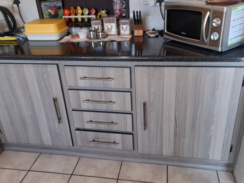A functional kitchen section featuring modern grey wood-grain laminate cabinetry, a dark granite countertop, and clean ceramic floor tiling.