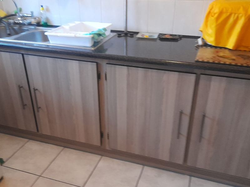A functional kitchen area featuring wood-look laminate cabinetry, dark granite countertops, and a double bowl stainless steel sink with tiled splashback.