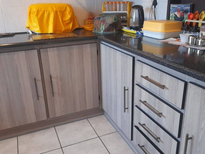 A functional kitchen area featuring modern wood-look laminate cabinetry, dark granite countertops, and clean ceramic floor tiling.
